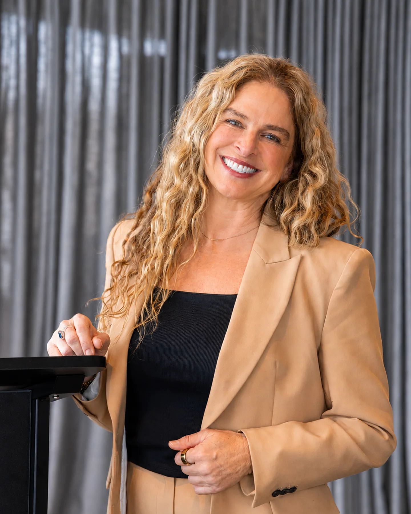 Dr Rebecca Chabot smiling beside a lectern in a tan blazer